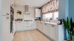 A modern kitchen with white cabinetry, a built-in oven, and a window with a patterned blind.