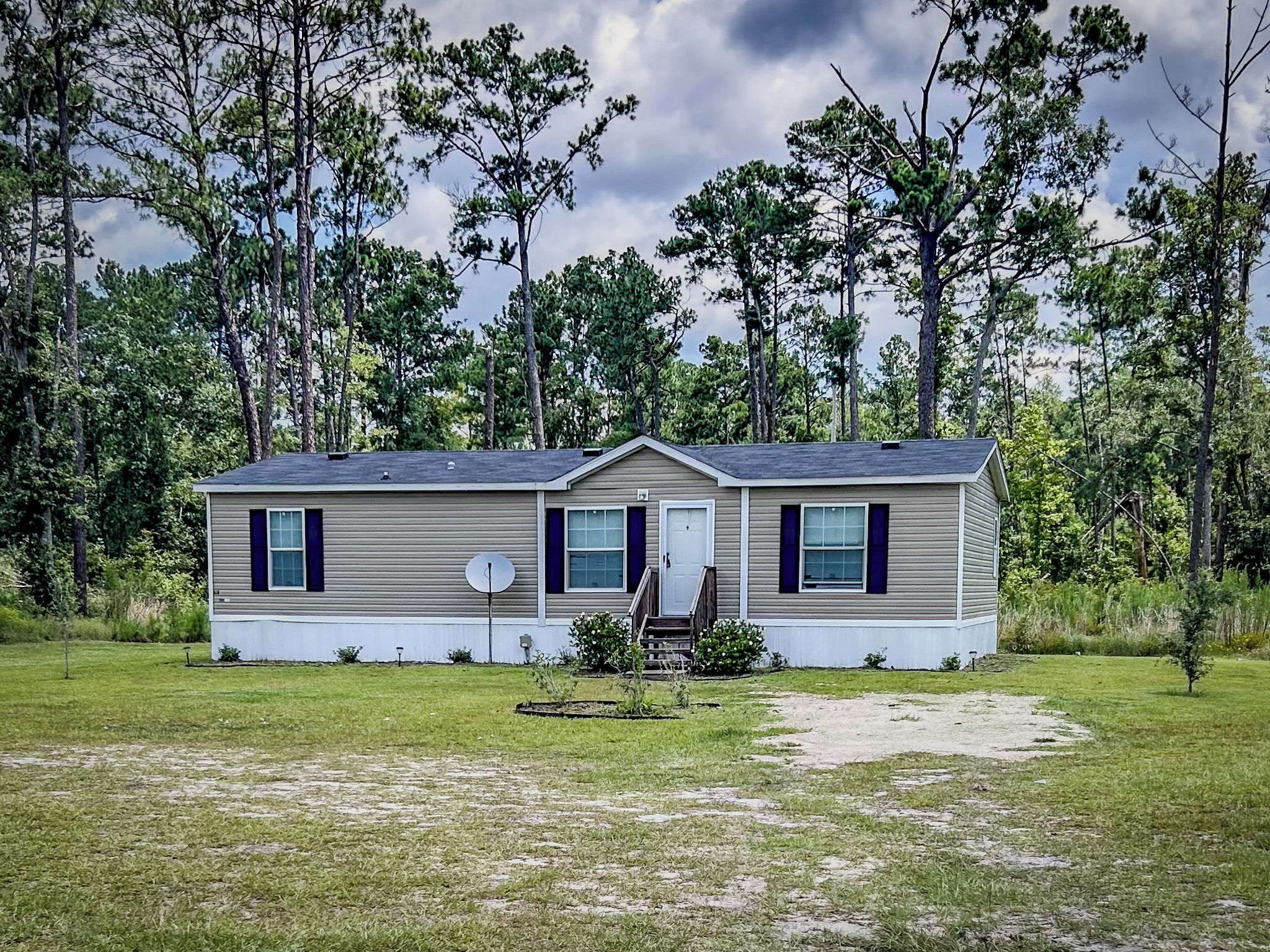 A single-story mobile home with a front porch, a satellite dish, and a small garden area.