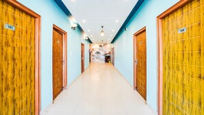 A hotel hallway with wooden doors numbered 101 and 108, leading to a room with a fan and a decorative wall. - Cozy Stays Near Doon University, Dehradun (Dehradun)