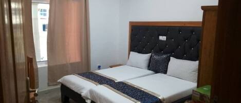 Una cama doble con cabecera capitonada, dos mesitas de noche y una ventana con cortinas.