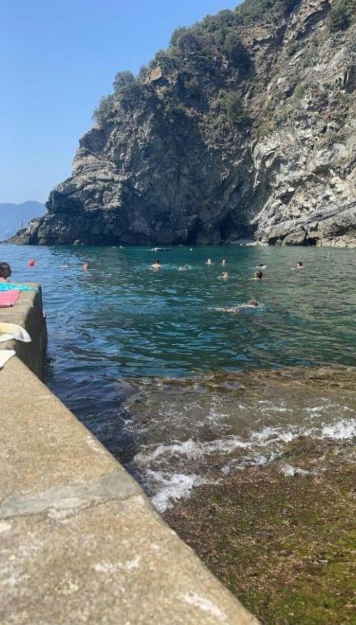 Eine felsige Küste mit klarem Wasser und badenden Personen.