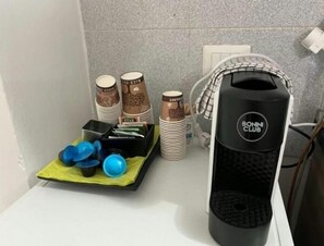 En köksbänk med en kaffemaskin, staplade koppar och ett fat med bestick.