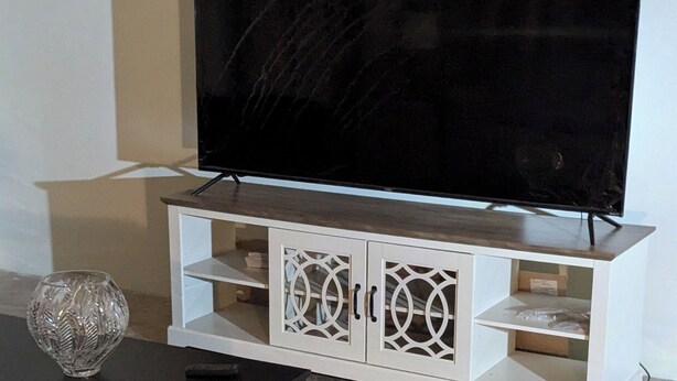 Una sala de estar con un televisor de pantalla plana sobre un mueble blanco, un aparador de madera oscura y una alfombra estampada.