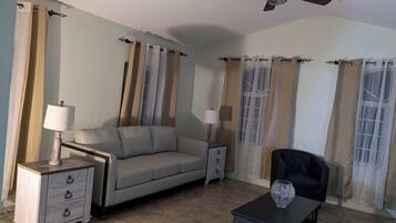 Ein Wohnzimmer mit einer Couch, zwei Nachttischen mit Lampen, einem Deckenventilator und Vorhängen.