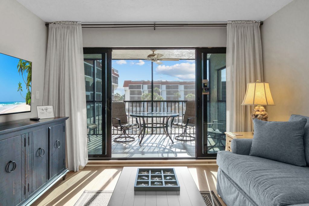 Una sala moderna con sofá, televisión, mesa de comedor con sillas y un balcón con vistas a edificios y palmeras.