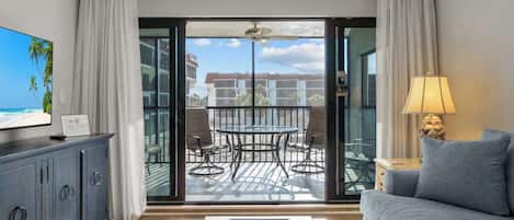 Una sala moderna con sofá, televisión, mesa de comedor con sillas y un balcón con vistas a edificios y palmeras.