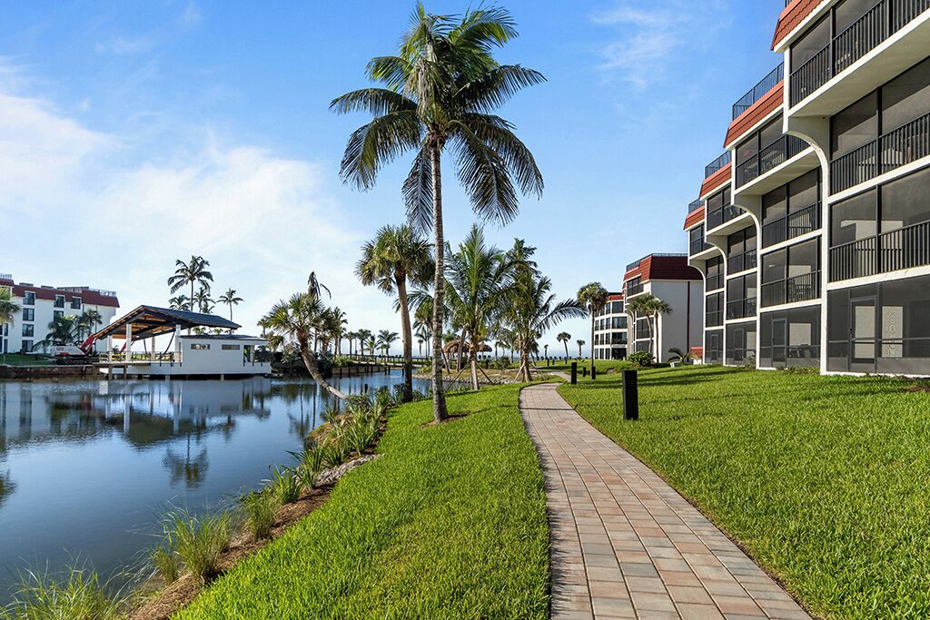 A waterfront hotel with a pathway, palm trees, and a body of water.