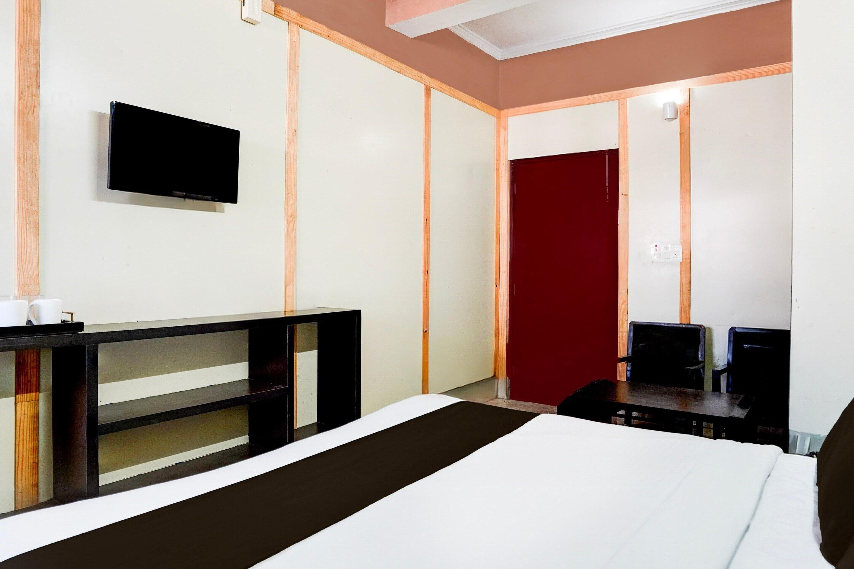 A hotel room with a bed, a TV mounted on the wall, a desk with a chair, and a red door.