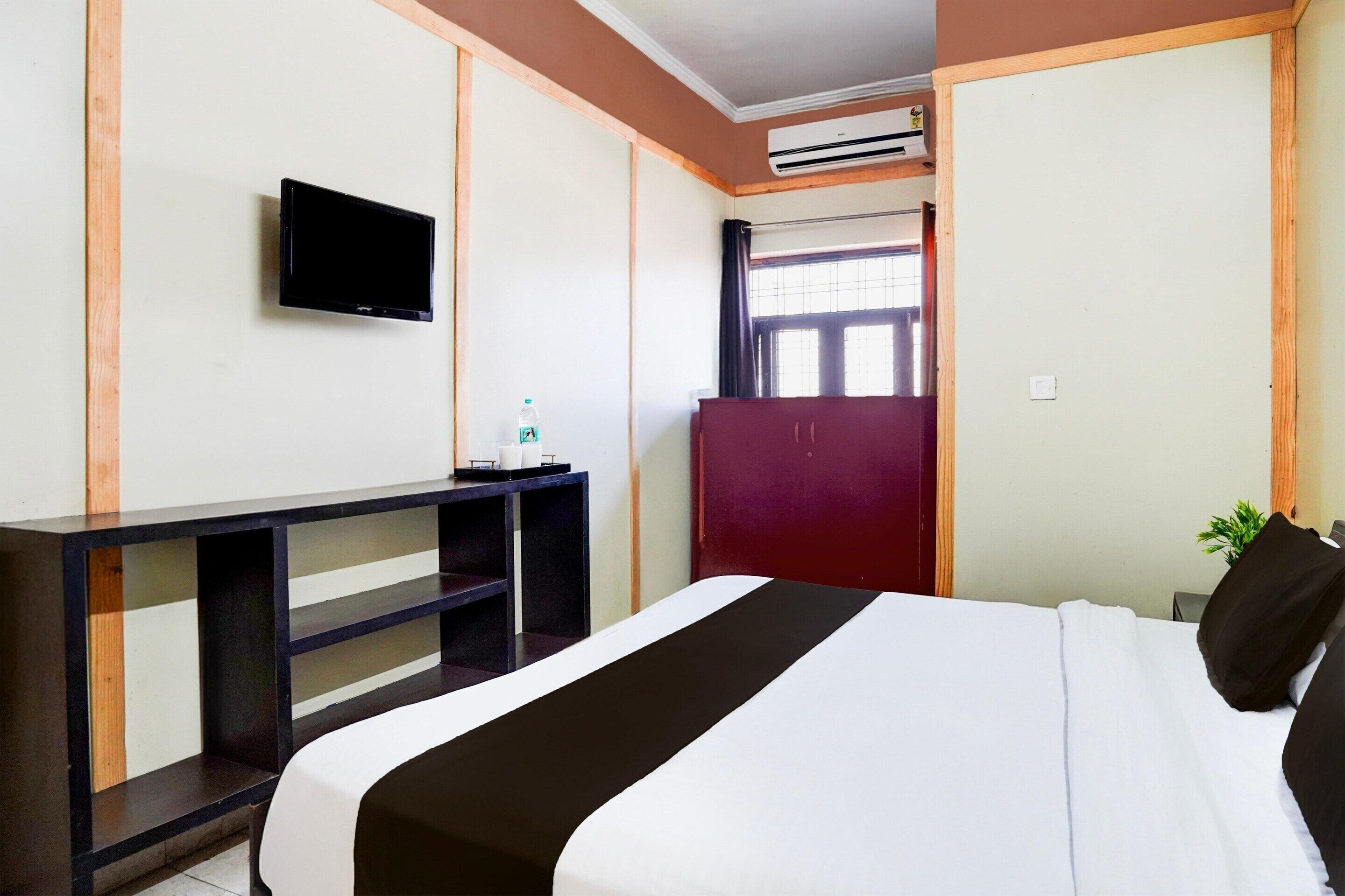 A hotel room with a bed, a TV mounted on the wall, a wardrobe, and a window with curtains.