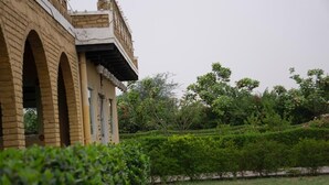 A building with arched windows and a garden with neatly trimmed hedges. - Sultanpur Resorts (Gurugram)