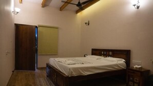 A bedroom with a wooden bed, a nightstand, a wall-mounted lamp, and a ceiling fan. - Sultanpur Resorts (Gurugram)