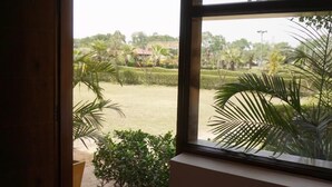 A room with a large window offering a view of a well-maintained garden and distant buildings. - Sultanpur Resorts (Gurugram)