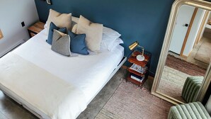 Een slaapkamer met een groot bed, een nachtkastje met een lamp, een spiegel en een groene stoel.