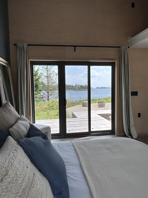 Ein Schlafzimmer mit einem großen Bett, Seeblick und einer Holzterrasse.