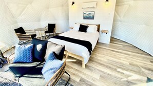 A cozy room with a bed, a chair, a small table, and a wall-mounted air conditioner.