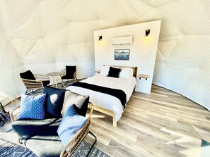 Ein gemütliches Zimmer mit einem Bett, einem Sessel, einem kleinen Tisch und einer Wand-Klimaanlage.