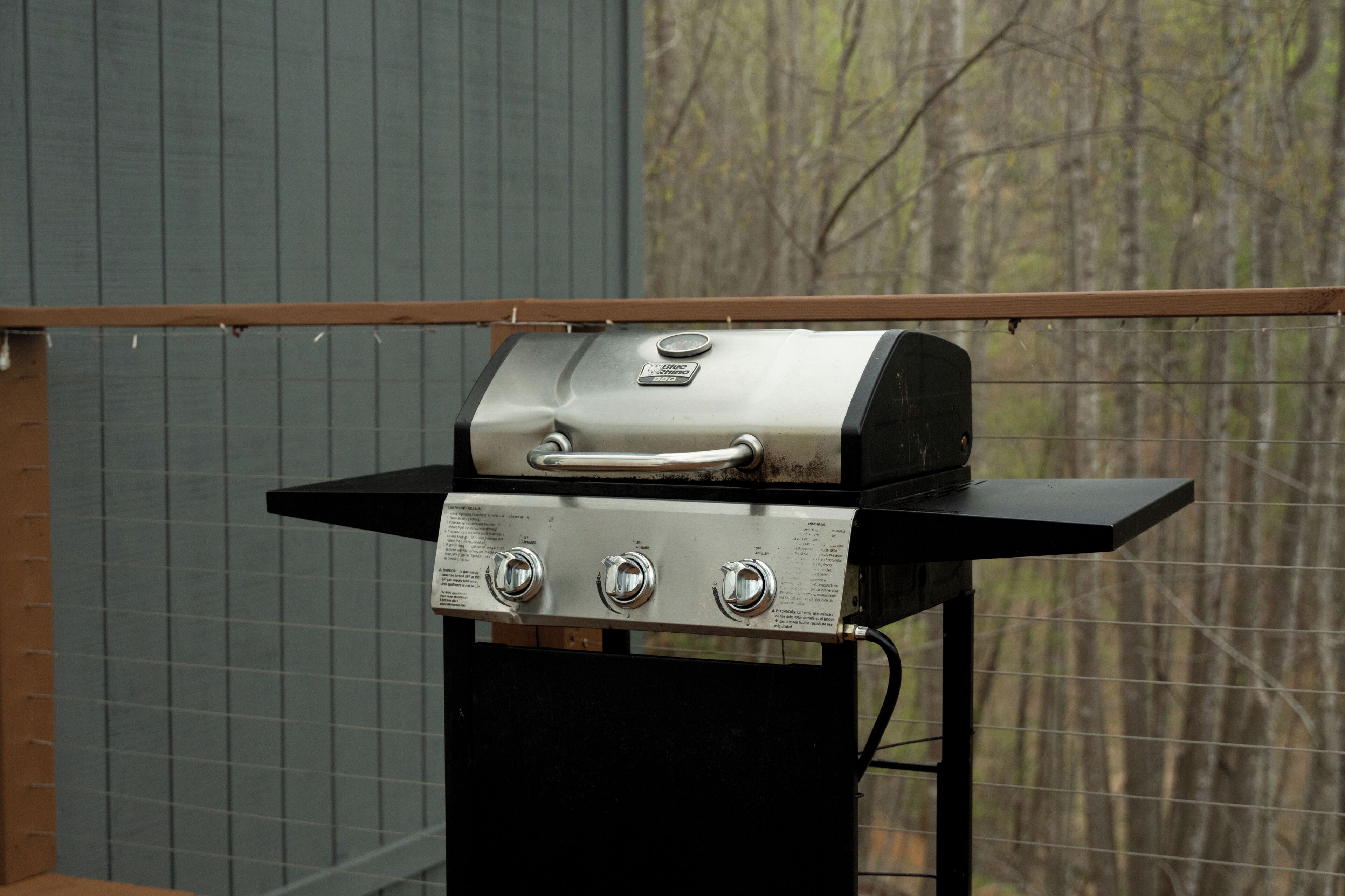 A portable gas grill with four burners, a thermometer, and a control knob, mounted on a black stand.
