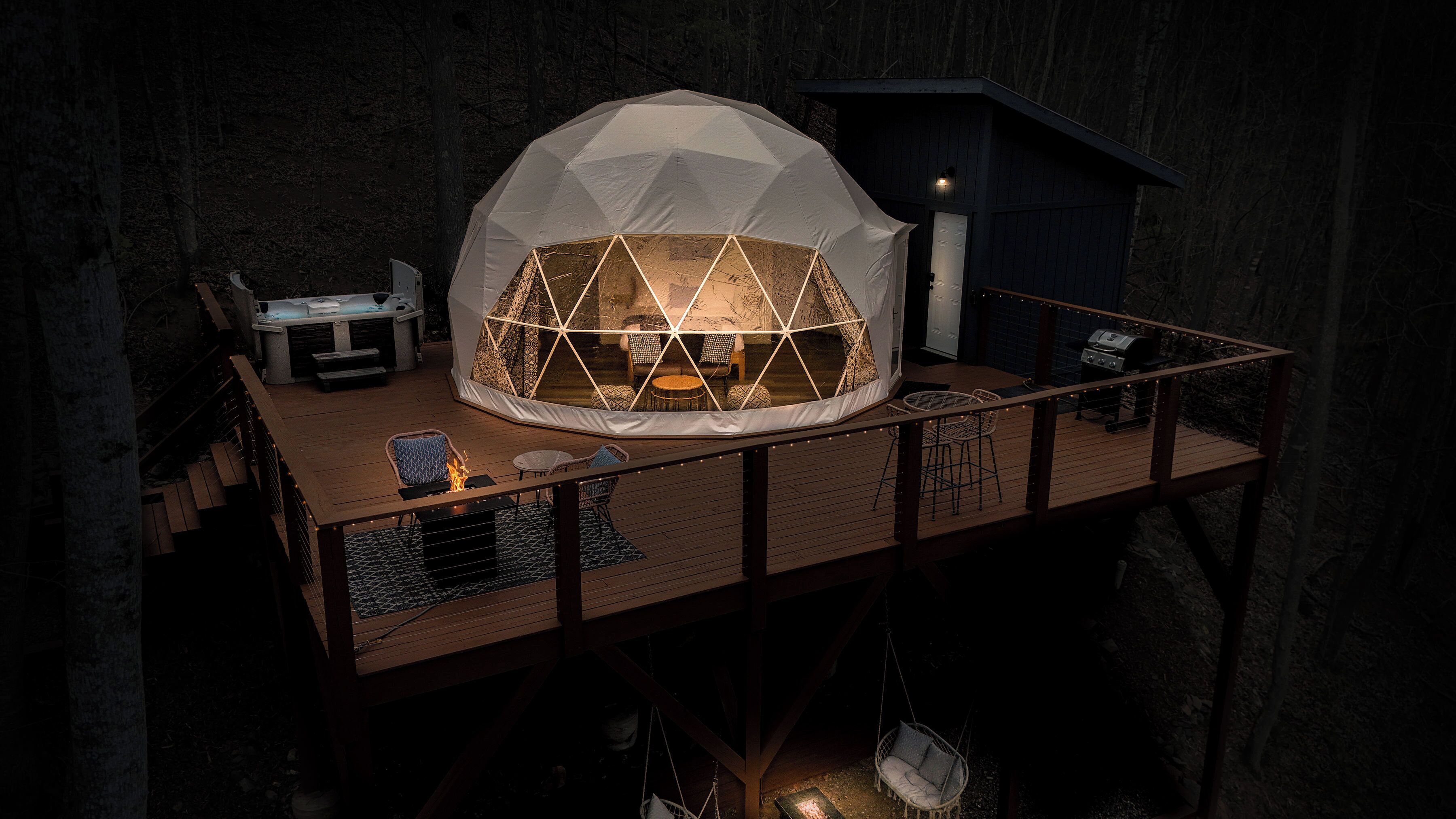 A geodesic dome structure with a fire feature, seating, and a grill on a wooden deck.