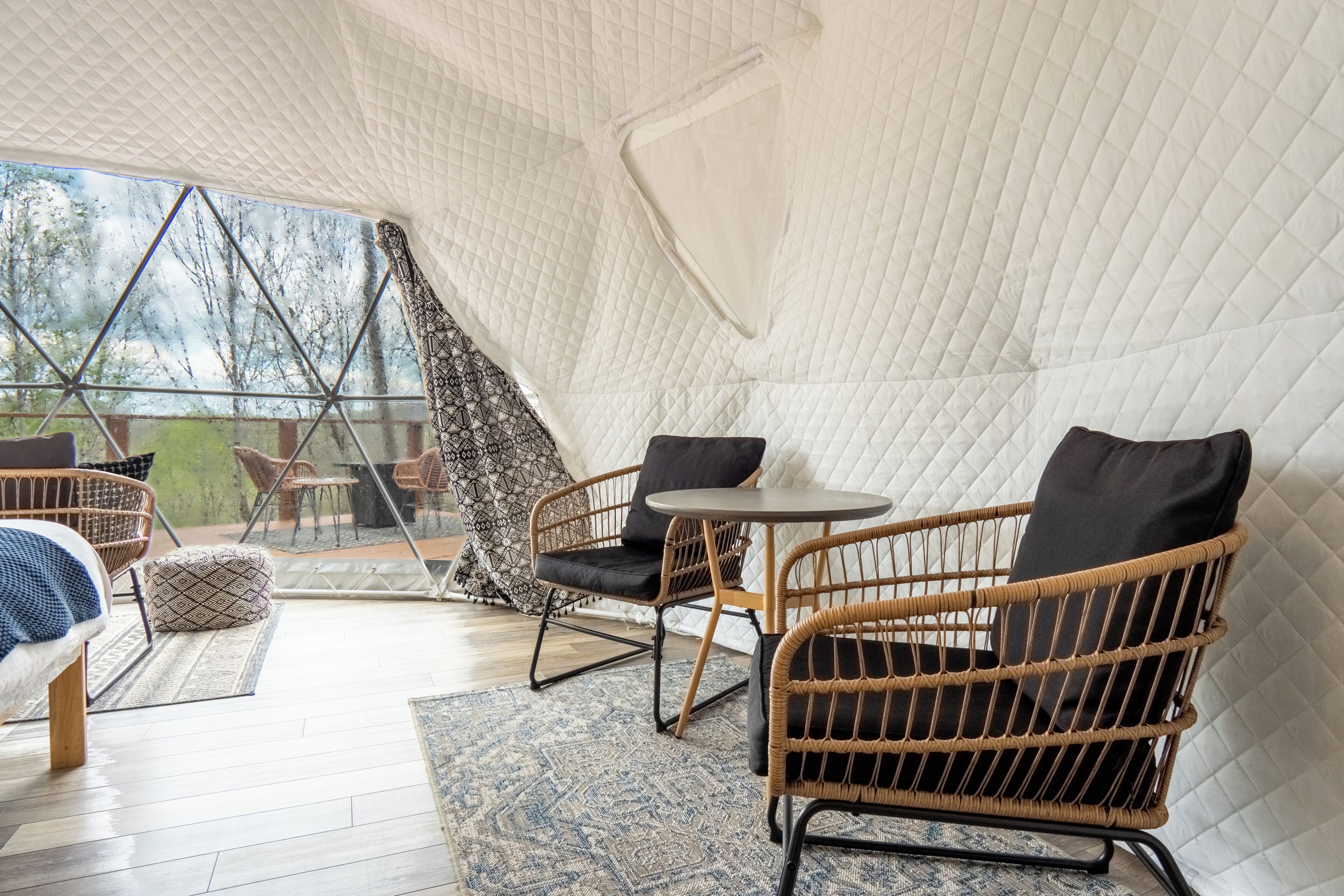 An indoor space with a high ceiling, wicker furniture, a small round table, and a view through a glass wall.