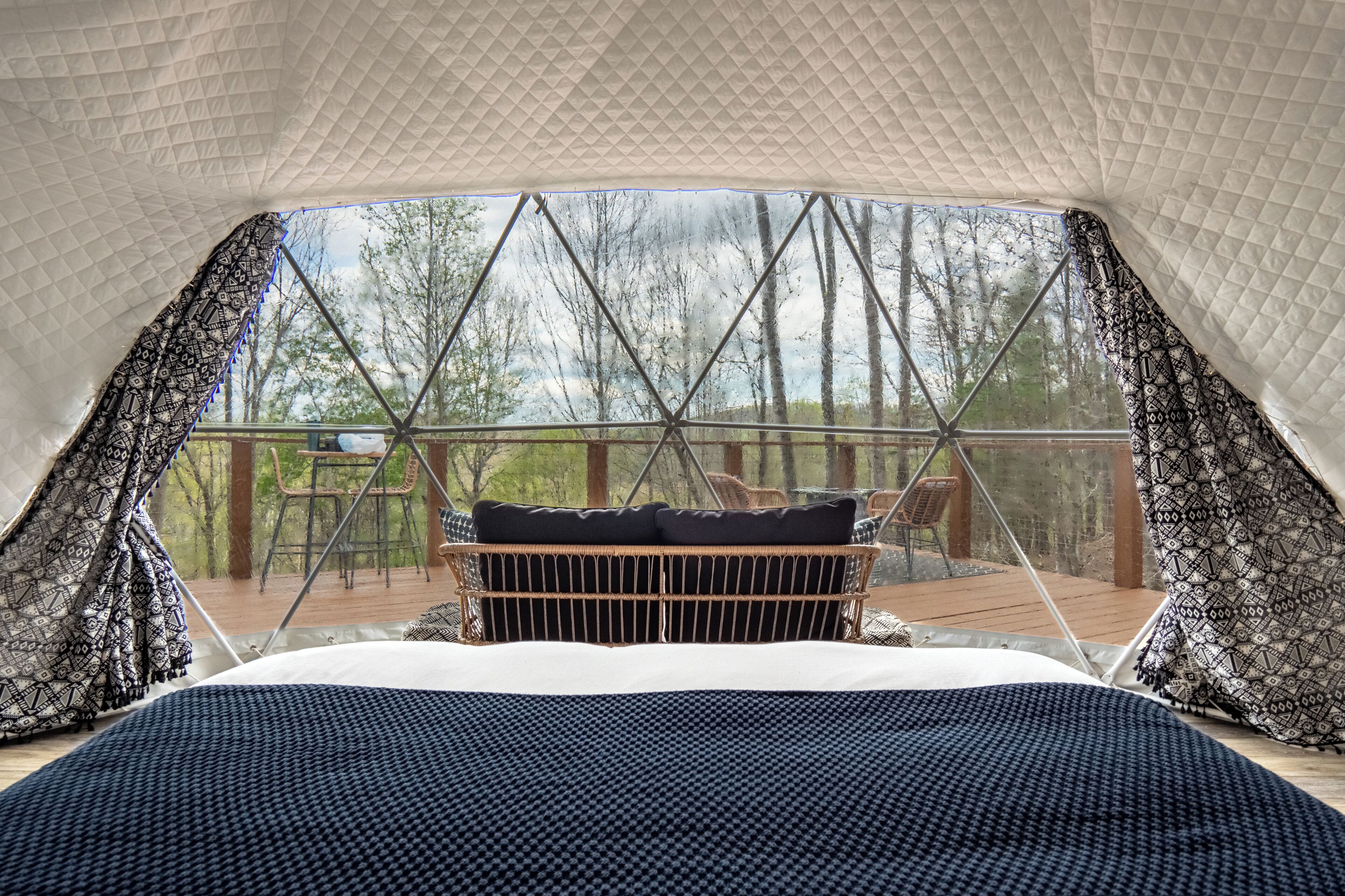 Eine Zelthütte mit Bett, Blick auf Bäume und einer Terrasse mit Stühlen.