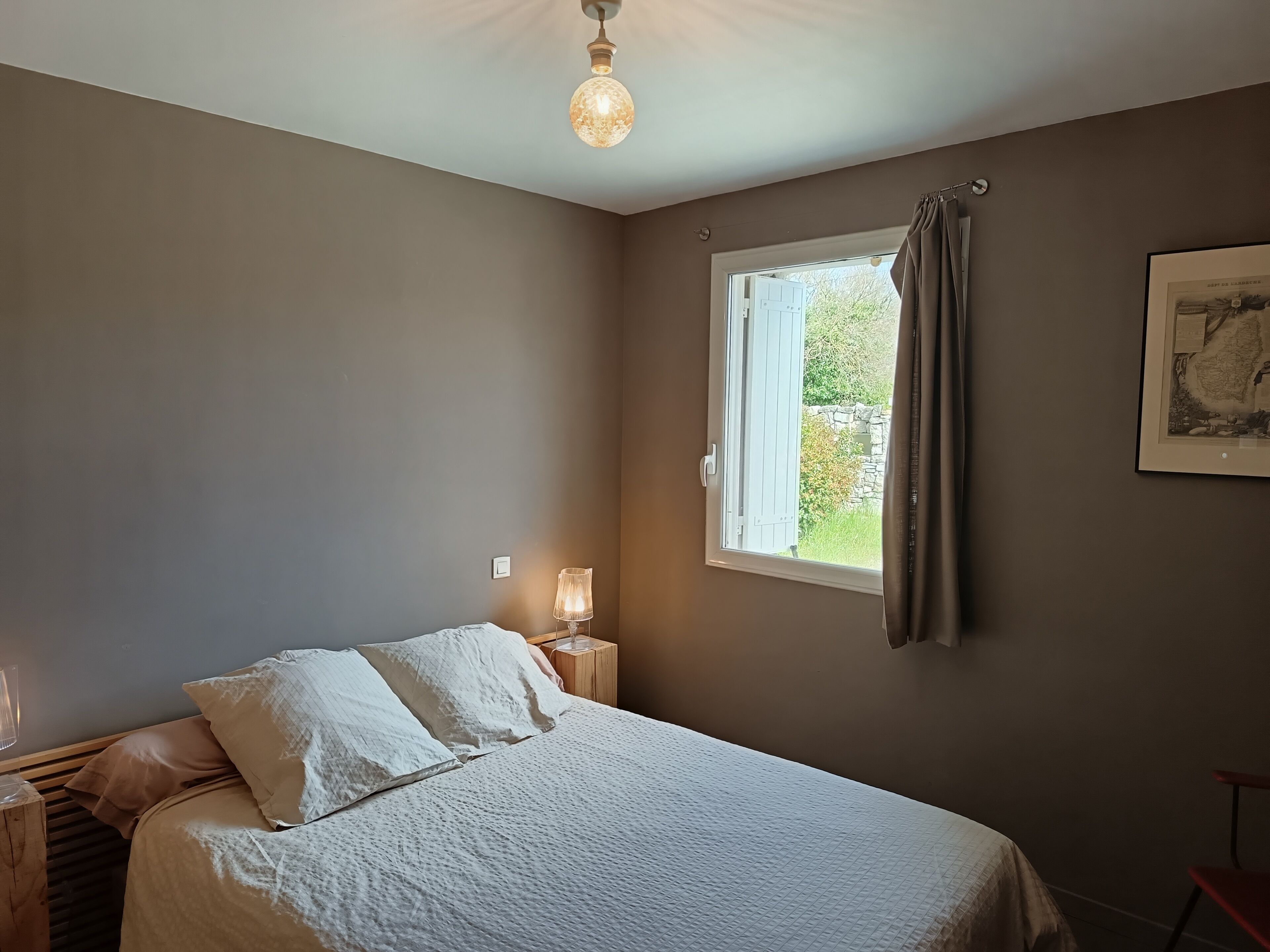 Une chambre à coucher avec un lit, une lampe de chevet, une fenêtre avec des rideaux et un tableau encadré au mur.