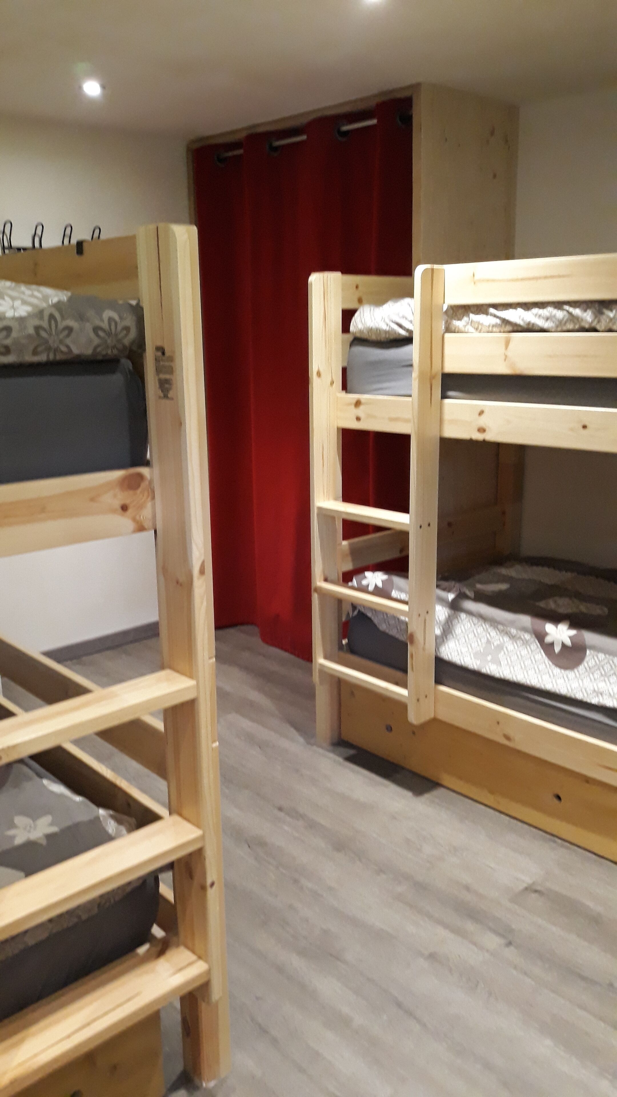 A room with two bunk beds, a red curtain, and a wooden floor.