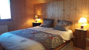 Een slaapkamer met houten lambrisering, een bed, twee bedlampjes en een raam.