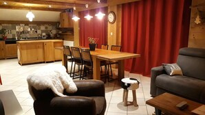 Een knusse woonkamer met een eethoek, een keuken op de achtergrond en een rood gordijn.