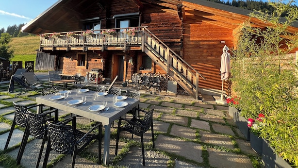 Een houten chalet met een balkon, buitenmeubels en een pad van stenen.