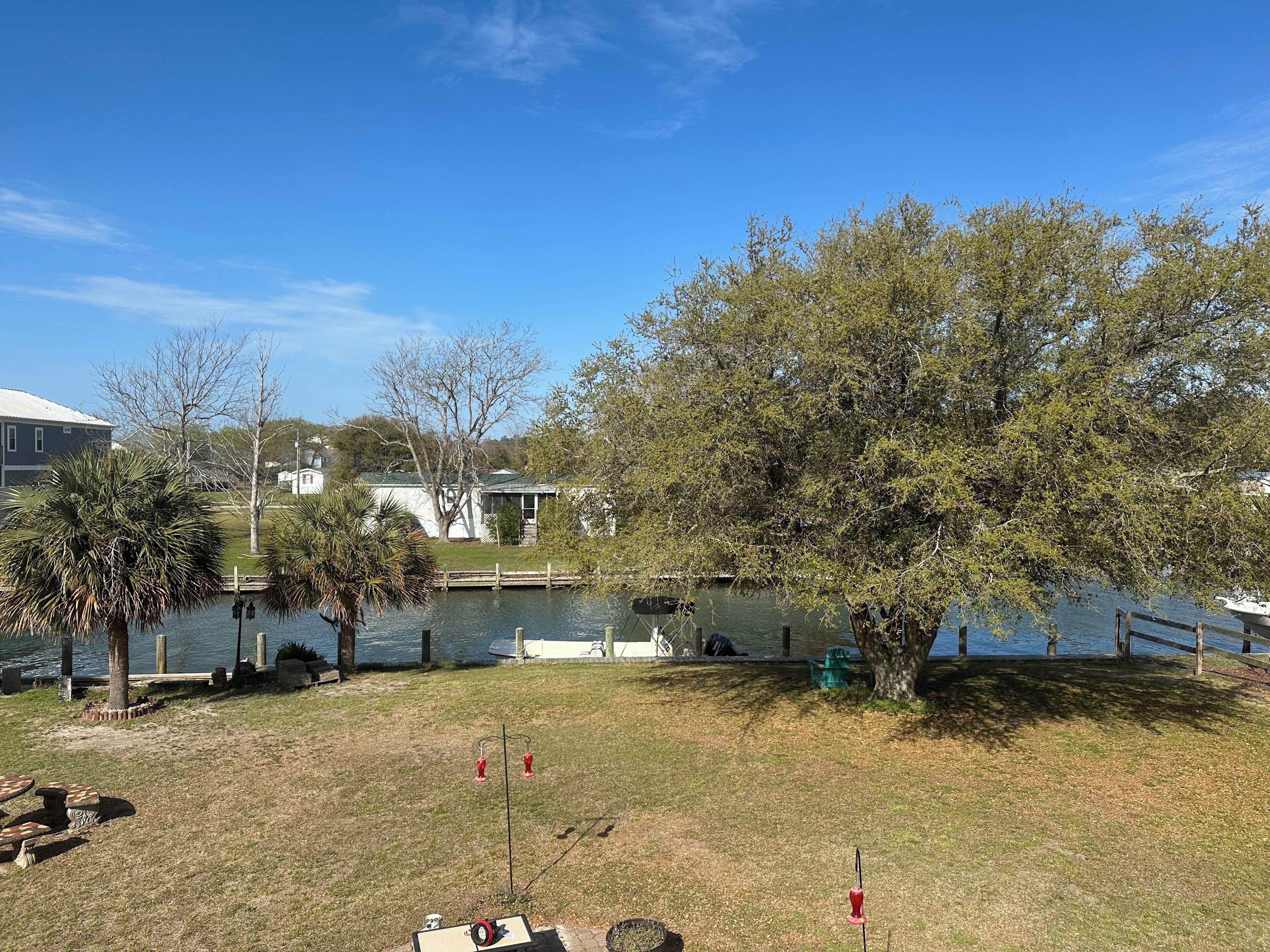 A lakeside view with a dock, trees, and a grassy area with outdoor furniture.