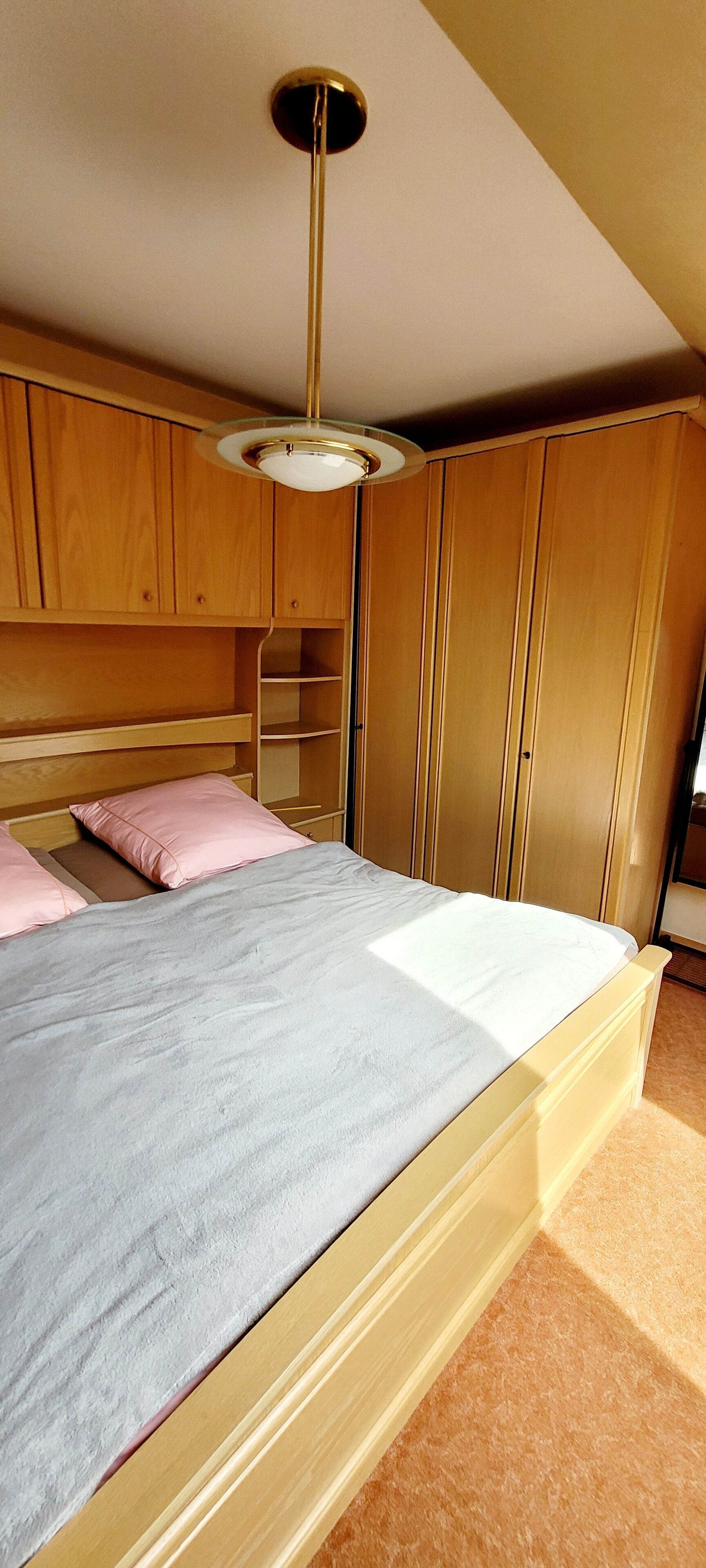 Ein Schlafzimmer mit Bett, Holzschrank und Deckenleuchte.