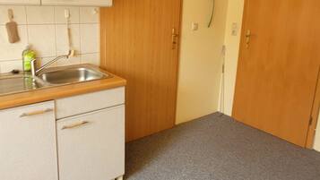 Une cuisine de taille réduite, équipée d’un évier, de placards et d’une porte en bois.