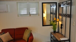 Un salon avec un canapé rouge, une petite table sur laquelle est posée une plante, un miroir et une lampe fixée au mur.