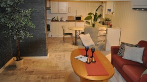 Un espace de vie compact comprenant un coin repas, une kitchenette et un coin salon avec un canapé rouge et une table en bois.