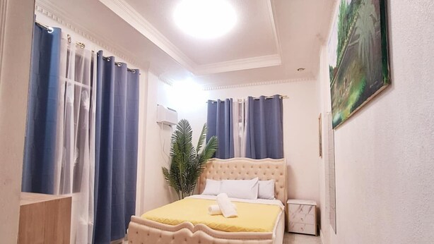 Une chambre à coucher avec un lit, des rideaux, une plante en pot et un tableau accroché au mur.
