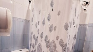 Une salle de bain équipée d’un rideau de douche orné d’un motif de feuilles, de toilettes, d’un lavabo et d’un distributeur de serviettes.