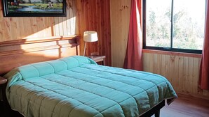 A wooden cabin room with a bed, a painting, a lamp, and a window. - Calafquen adventure Hostel y cabañas (Conaripe)