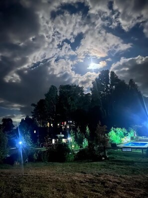 Ein Haus bei Nacht mit Swimmingpool, umgeben von Bäumen und beleuchtet von Straßenlaternen.