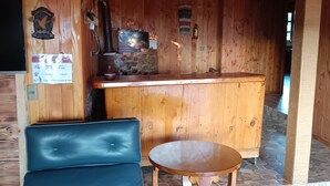A wooden cabin interior with a black leather sofa, a wooden table, a stone fireplace, and a wooden bar counter. - Calafquen adventure Hostel y cabañas (Conaripe)