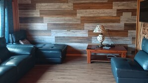 A living room with a herringbone-patterned wooden wall, two black leather sofas, a wooden coffee table, and a lamp. - Calafquen adventure Hostel y cabañas (Conaripe)