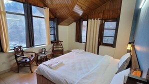 Ein gemütliches Schlafzimmer mit Holzboden, einem großen Bett, einem Schreibtisch mit Lampe und Blick ins Freie durch die Fenster.