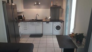 Une cuisine compacte équipée d’un lave-vaisselle, d’une machine à laver et d’un four à micro-ondes. On y trouve une petite table à manger et une plante en pot.