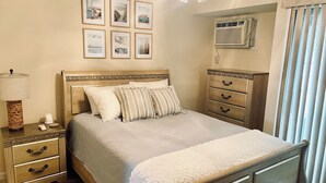 A neatly arranged bedroom with a bed, bedside tables, a dresser, and a wall-mounted air conditioner.