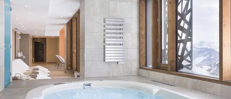 A modern indoor swimming pool with a view of snow-capped mountains through large windows.