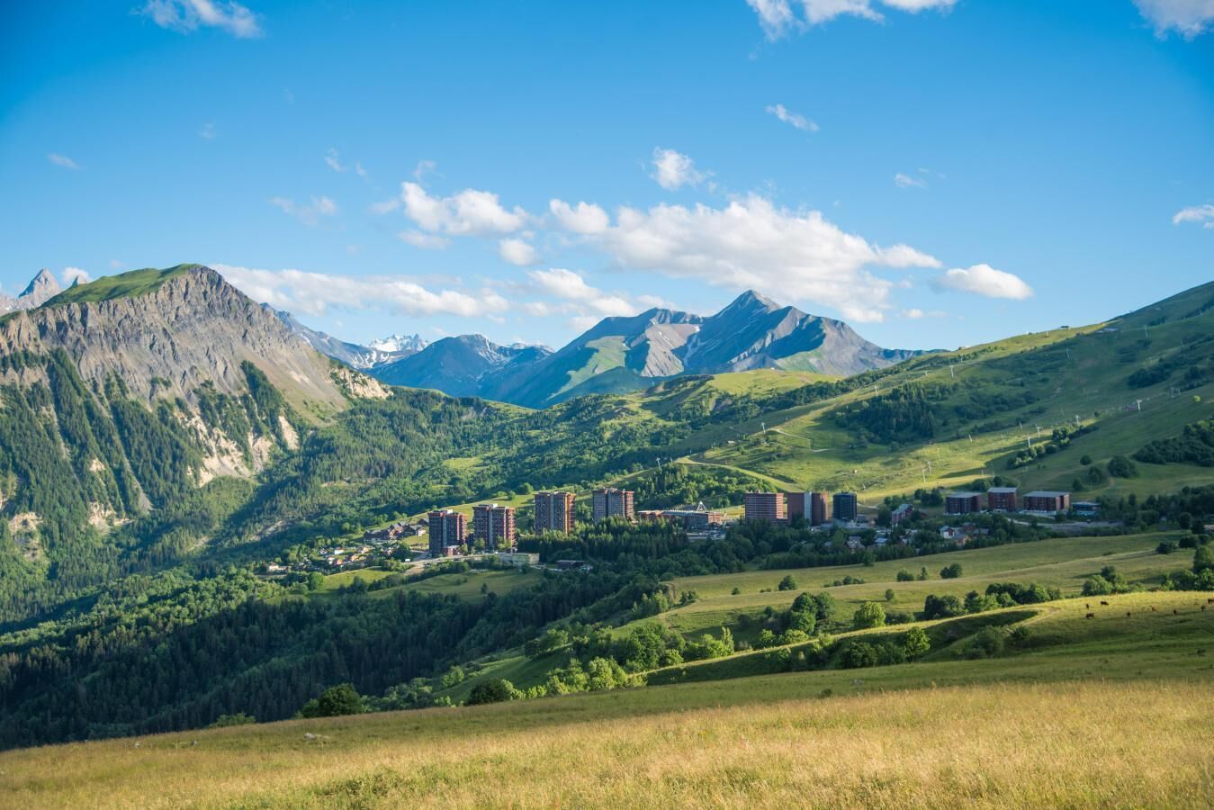 Paesaggio montuoso con un gruppo di edifici, probabilmente un albergo, immerso tra dolci colline e montagne.