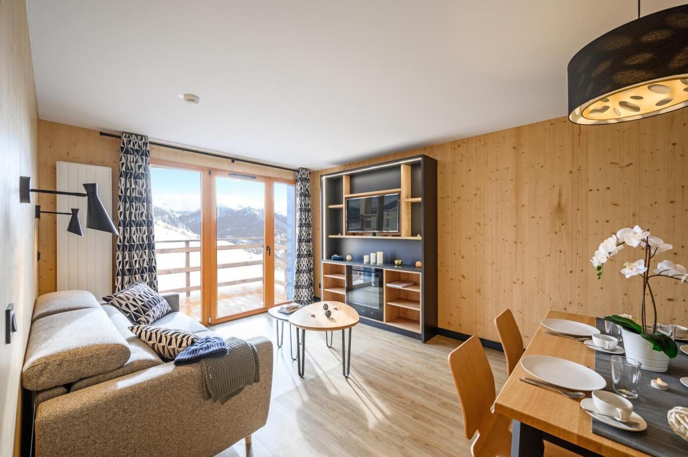 Un soggiorno moderno con un divano, un tavolo da pranzo con sedie, una TV e vista sulle montagne attraverso le porte scorrevoli in vetro.