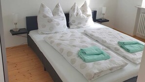 A neatly made bed with white bedding and teal towels, two bedside tables with lamps, and a wooden floor. - Vacation apartment Weinstraßenmitte (Neustadt an der Weinstraße)