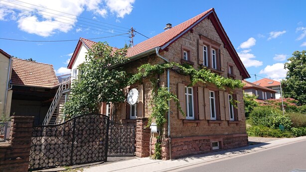 A two-story stone house with a red-tiled roof, a metal gate, and a satellite dish. - Vacation apartment Weinstraßenmitte (Neustadt an der Weinstraße)