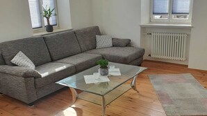 A modern living room with a grey sofa, a glass coffee table, and a wooden floor. - Vacation apartment Weinstraßenmitte (Neustadt an der Weinstraße)