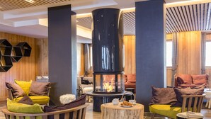 A cozy lounge area with a central wood-burning stove, comfortable seating, and a wooden wall. - Apartment in Tignes With Ski-in/ski-out Access (Tignes)